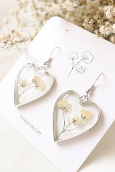 two silver heart shaped earrings with flowers on them sitting next to a card and some dried flowers