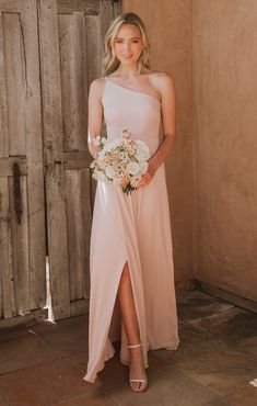 a woman standing in front of a wooden door wearing a pink dress and holding a bouquet