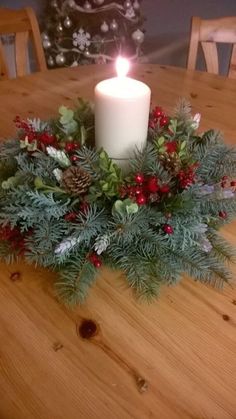 a candle sitting on top of a wooden table next to a wreath filled with berries and pine cones