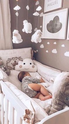 a baby sleeping in a crib with clouds hanging from the ceiling and stuffed animals on the wall