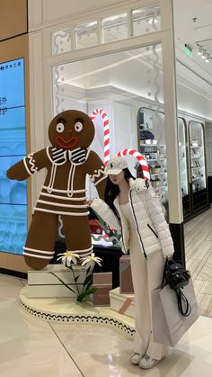 a woman standing next to a giant gingerbread man in a shopping mall with candy canes