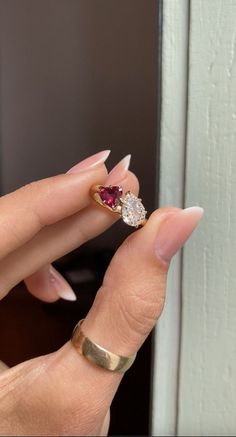 a woman's hand holding a gold ring with two diamonds and a red stone