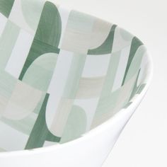 a close up of a bowl on a white surface with green and beige designs in it