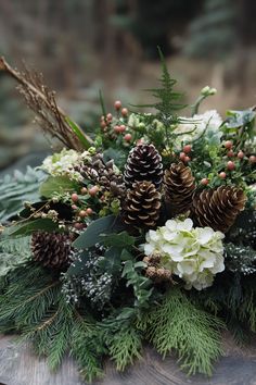 a bouquet of flowers and pine cones sitting on top of a wooden table covered in greenery