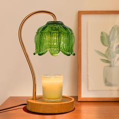 a green glass lamp sitting on top of a wooden table next to a lit candle