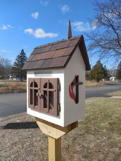 a small white house with a cross on the roof and window panes in front of it