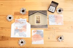 the wedding stationery is laid out on top of the wooden table with flowers and rings