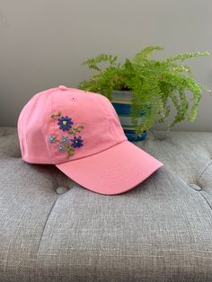 This listing is for one hand embroidered baseball cap.  Blue and periwinkle flowers on spring green stems embroidered on a petal pink cap. Each of my PetalStitch baseball cap designs is unique and one of a kind.  They are inspired by the beautiful wildflowers we have here in Wisconsin in our backyards and in the countryside.  I'm constantly designing new caps, so please check back often to see new listings.  Hats are a cotton "one size fits most" and can be sized with the adjustable metal slider on the back.  If you have any specific questions regarding the hats, please reach out to me via Etsy messages. This hat is ready to ship and will ship free via USPS first class mail.  Priority mail is available as an upgrade at checkout.  Please note that you will be provided with a tracking number Pink Baseball Hat, Periwinkle Flowers, Pink Cap, Cap Designs, Embroidered Hat, Embroidered Baseball, Embroidered Baseball Caps, Embroidered Hats, Backyards