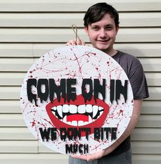 a young man holding up a sign that says come on in we don't bite me