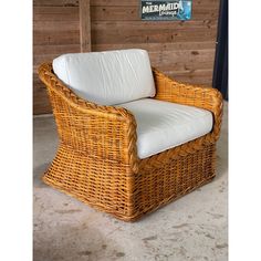 a wicker chair with white cushions in front of a wooden wall and sign that reads mermaid