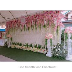 an outdoor wedding setup with pink and white flowers on the wall, along with greenery