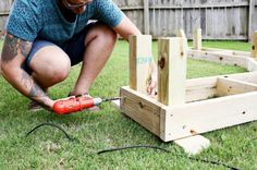 a man working on some wooden posts in the grass with an electric drill and power tool