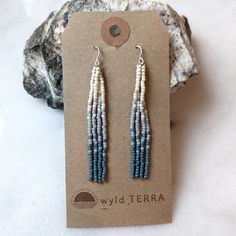 the blue and white beaded earrings are displayed on top of a card next to a rock