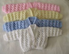 four knitted sweaters laid out on a bed