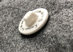 a white button with writing on it sitting on top of a gray carpeted floor