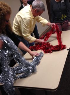 some people are doing something with tinsel on the table and one person is cutting it