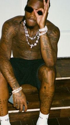 a man sitting on the floor with his hands to his face and tattoos on his body