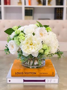 white flowers in a glass vase on top of two books