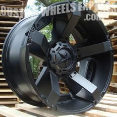 an image of a black wheel that is on some pallets in the background with trees and wood behind it