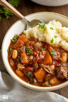 a white bowl filled with stew and mashed potatoes on top of a wooden table