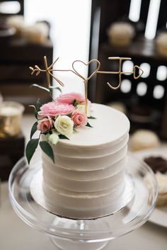 a white cake with flowers and initials on top is sitting on a clear platter