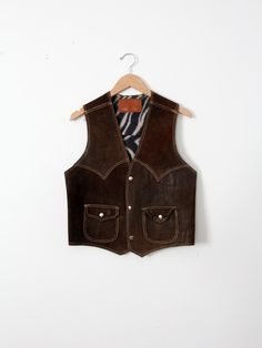 "This is a 1970s vintage suede leather vest. Dark brown suede shapes the vest with tan top-stitching. It features snap pockets on the waist, and snaps closed. The interior has a zebra print lining. CONDITION In good condition with wear consistent with age and use. Fantastic natural wear and patina to the leather. Approximate Size: Men's Small / Medium  MEASUREMENTS Bust:           38\"  ...         96.5 cm Length:       20\"      ...          50.8 cm Shoulders: 13.5\"      ...        34.3 cm HOW Cowboy Vest, Leather Biker Vest, Looks Country, Biker Vest, Brown Vest, Suede Vest, Men Suede, Tan Top, Vintage Suede