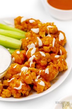 a white plate topped with cauliflower covered in ranch dressing and celery sticks