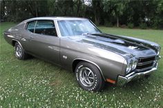 an old muscle car parked in the grass