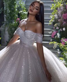 a beautiful woman in a white dress posing for the camera with flowers on the stairs behind her