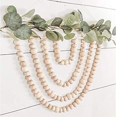 three strands of white wood beads with green leaves hanging from the side on a wall