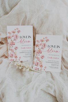 two wedding cards laying on top of a white bed with pink flowers in the middle