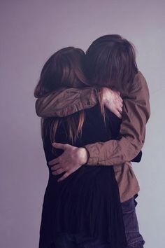 two people hugging each other in front of a white wall