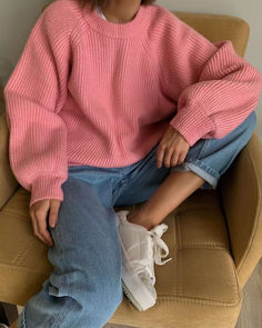 a woman sitting on top of a chair wearing a pink sweater and white tennis shoes