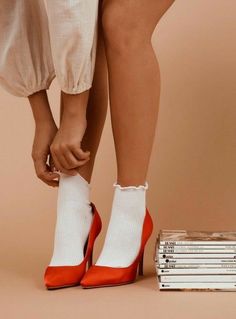 a woman's legs with red and white shoes next to stack of books