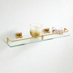 a glass shelf with a candle and soap dispenser on it in front of a white brick wall