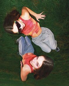 two young women laying on the grass with their hands in each other's pockets