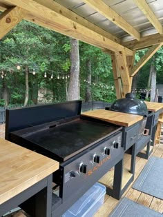 an outdoor kitchen with grills and picnic tables on the deck in front of trees