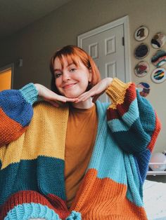 a woman with red hair wearing a multicolored knitted sweater and smiling at the camera