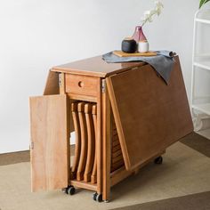 a small wooden table with an open drawer on wheels and a vase sitting on top of it