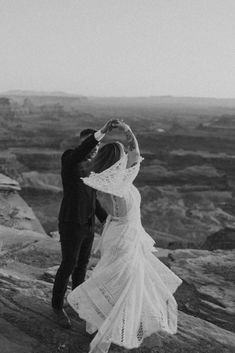 a bride and groom kissing on top of a mountain in black and white, with the sun behind them