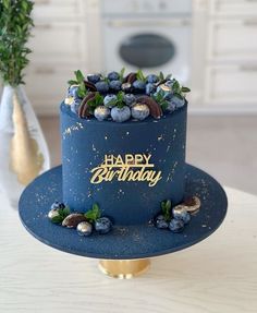 a birthday cake with blueberries and nuts on top sits on a table in front of a potted plant