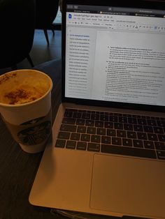 an open laptop computer sitting on top of a wooden table next to a cup of coffee