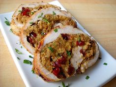 three slices of meat with cranberries and herbs on a white plate sitting on a wooden table