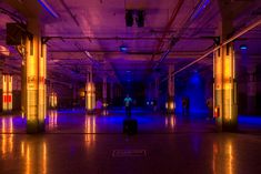 people are standing in an empty building with purple and blue lights on the ceiling, while one person is carrying a suitcase