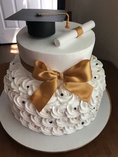 a graduation cake decorated with white icing and gold ribbon