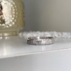 Our Cora Vintage Band is reminiscent of the old-world wedding bands of the past. It's a perfect addition to your ring stack! Mix and match from our collection of simple to delicately detailed bands. All designed to look perfect worn together in whatever combination you choose to create! This ring is hand-made in our studio at the time of order of sterling silver. Choose from a bright silver finish or oxidized to bring out the detail in the design, 4mm wide band. You're going to love creating you Timeless Stackable Engraved Wedding Ring, Classic Stackable Toe Rings, Timeless Engraved Ring With Decorative Band As Gift, Timeless Stackable Engraved Ring For Anniversary, Elegant Stackable Adjustable Engraved Ring, Elegant Adjustable Stackable Engraved Ring, White Gold Heirloom Stackable Rings, Classic Engraved Stackable Promise Ring, Classic Stackable Engraved Promise Ring