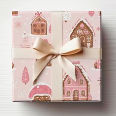 a present wrapped in pink and white paper with a gold bow on the top that is decorated with gingerbread houses