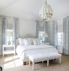 a white bed sitting in a bedroom next to two windows with blue drapes on them