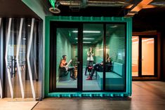 two people sitting on a bench in front of a green shipping container with glass doors