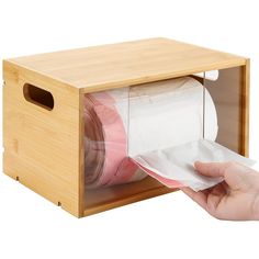 a person holding a roll of toilet paper in a wooden box